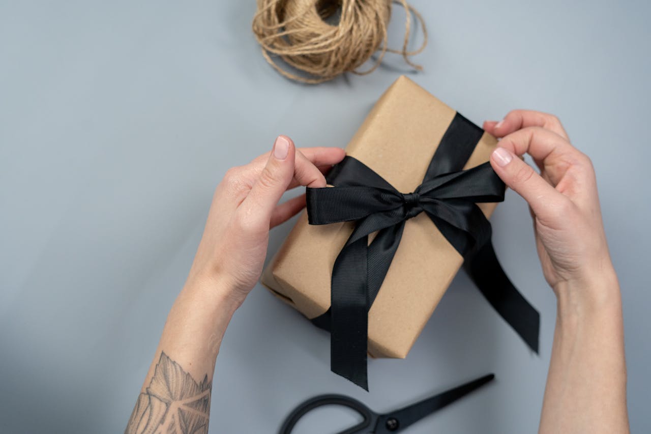 Close-up of hands wrapping a gift box with a black ribbon, ready for gifting.
